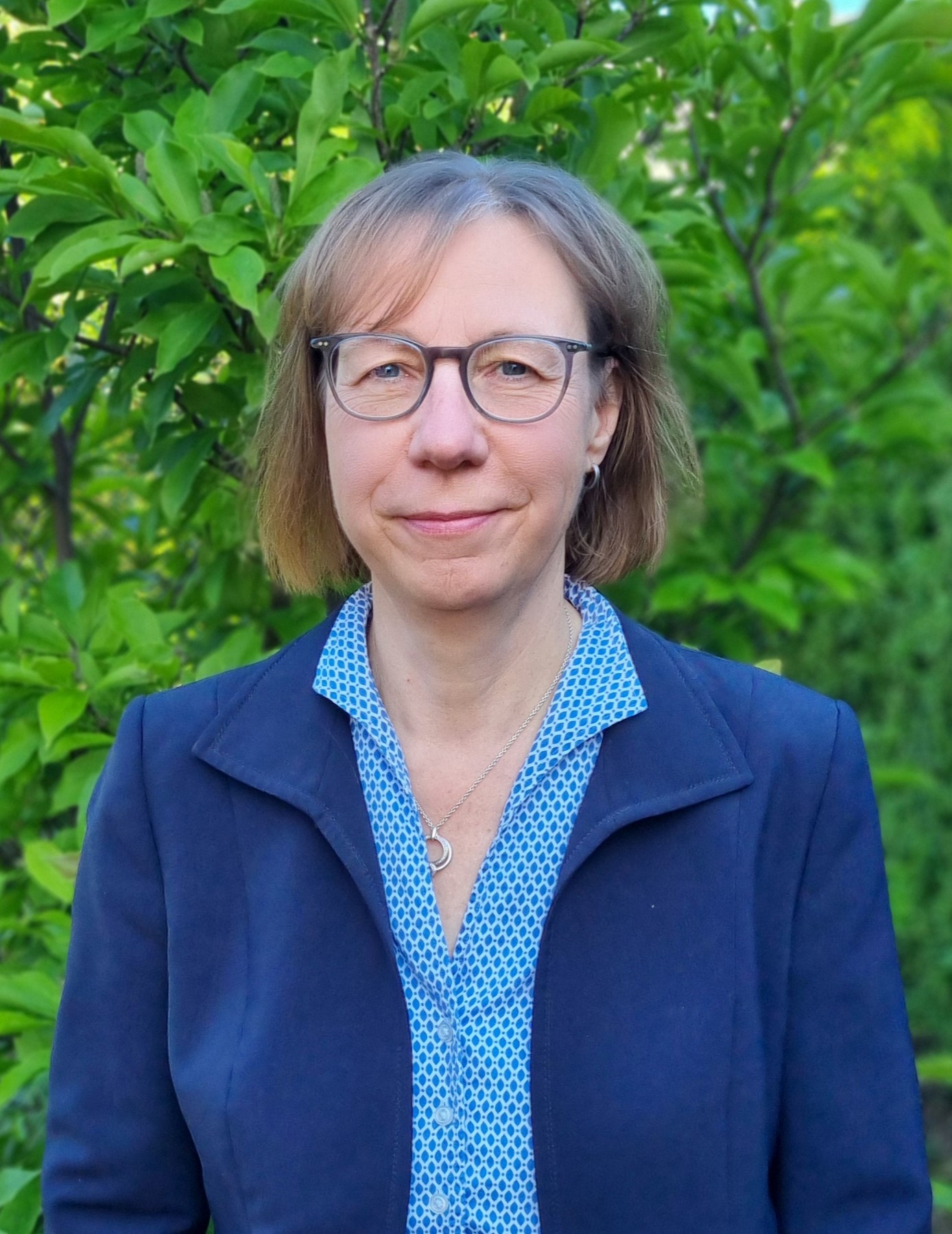 Frau mit Brille vor einen grünen Naturhintergrund