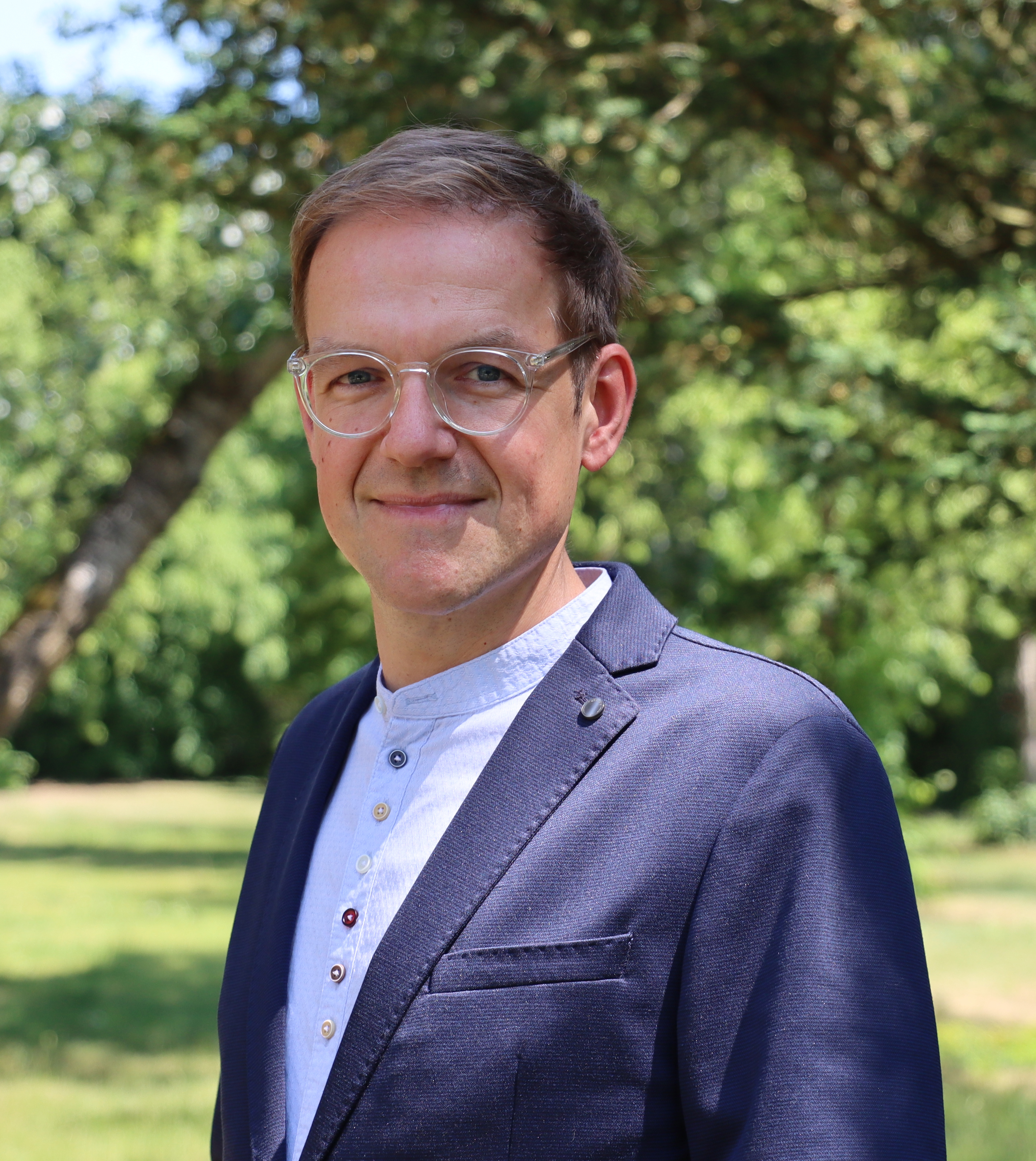 Mann mit Brille und blauem Sakko lächelt freundlich in die Kamera