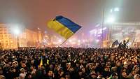 Mehrere Tausend Menschen während einer Demonstration, eine Frau in der Menge schwenkt die Ukrainische Flagge.