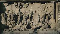 In Stein gehauenes Relief. Römische Soldaten tragen Beutestücke aus dem Jerusalemer Tempel, etwa die siebenarmige Menora.