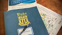 Tagungsmappe der INIRE-Tagung mit einem goldenen Logo der Duke-University#en auf blauem Hintergrund