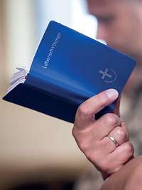 Hand eines Soldaten hält ein blaues Gebetsbuch mit dem Titel Lebensrhythmen