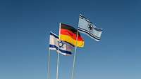 Israelische und deutsche Flagge mit Flagge der Übung Blue Flag (hellblau mit Davidstern) vor blauem Himmeln im Wind.