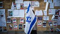 Eine israelische Frau mit einer Flagge des Landes vor einer Wand mit Plakaten der von der Hamas entführten Israelis.