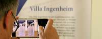 Hinterkopfansicht eines Mannes wie er mit dem Handy Plakate der Villa Ingenheim fotografiert