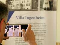 Hinterkopfansicht eines Mannes wie er mit dem Handy Plakate der Villa Ingenheim fotografiert