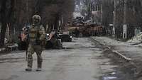 Ukrainische Soldaten patroulieren auf einer von zerstörten Panzern blockierten Straße in Butscha