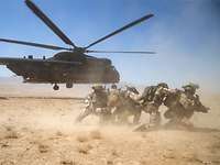 Soldaten schützen sich vor einem startenden Hubschrauber vor aufgewirbeltem Sand.