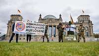 Demonstranten in Militäruniformen, Plakaten und Fahne stehen auf der Wiese vor dem deutschen Parlament