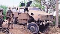 Soldaten stehen vor einem durch einen Sprengstoffanschlag zerstörten Dingo