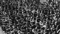 Eine Masse von Menschen zeigt den Hitlergruß, ein Einzelner in der Mitte verschränkt verweigernd die Arme vor der Brust.