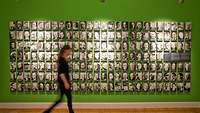 Eine Person läuft im Vordergrund an einer Wand mit zahlreichen Portraitfotos von Mitglieder des Widerstandes entlang