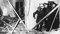 Hitler und Mussolini blicken in die zerstörten Überreste des Konferenzraums in der Wolfsschanze, der von Trümmern übersät ist.