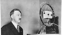 Hitler steht vor einem großen runden Rundfunk-Mikrofon, um eine Radioansprache zu halten.