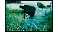 Ein Fotograf unter einem schwarzen Tuch mit Großformatkamera auf Stativ.