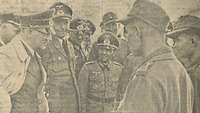Ein Foto aus einem Zeitungsausschnitt zeigt eine Gruppe von Männern in Uniformen im Gespräch