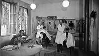 Bild des Friseursalons in der "Wolfsschanze", zwei Männern in Friseurstühlen werden die Haare geschnitten.