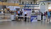 Messestand mit Menschen in Uniform und zivil Doppeldeckerflugzeuge im Hintergrund