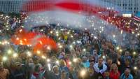 Eine Menschenmenge protestiert in Minsk mit Lichtern und Fahnen gegen die gefälschte Präsidentenwahl.