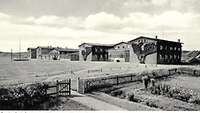 Foto in schwarz/weiß, sechs Gebäude mit Wiese 