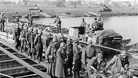 Pontonbrücke über Fluss mit Soldaten, Motorrad und Panzern, im Hintergrund Schlauchboote