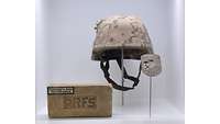 Gefechtshelm mit Helmbezug in Wüstenflecktarn davor ein Ziegelstein mit eingeprägtem Schriftzug