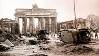 Vor dem Brandenburger Tor eine zerstörte Straße mit beschädigten und umgekippten Autos.