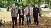 vier Männer unter Bäumen, zwei in Uniform zwei mit Sakko