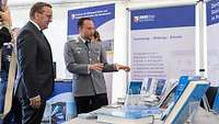 Ein Mann im Anzug und ein Mann in Uniform vor einem Büchertisch.