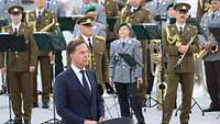 Mann im Anzug vor gemischter Militärkapelle. 