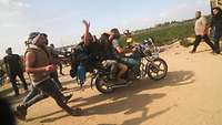 Terroristen der Hamas entführen eine Frau auf einem Motorrad, weitere Terroristen laufen daneben.