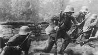 Vier deutsche Soldaten stürmen als Teil eines Stoßangriffs mit Gewehr in der Hand nach vorne.