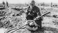 Australischer Soldat hockt auf der Erde und hält einen deutschen Flammenwerfer in der linken Hand.
