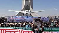 Eine ausgestellte Drohne im Iran vor einem Turmgebäude, davor eine Menschenmenge.