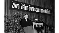 Verteidigungsminister Rühe hinter Rednerpult mit Bundesadler, oben der Banner Zwei Jahre Bundeswehr der Einheit