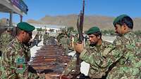Afghanische Soldaten zeigen eine Sammlung dutzender aufgereiht liegender eingesammelter Waffen.