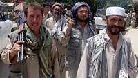 Afghanische Männer laufen eine Straße entlang, telweise tragen sie Waffen auf der Schulter.