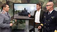 Zwei Soldaten und ein Mann stehen an einem Tisch vor einem Monitor und sprechen miteinander