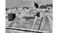 Sandburg mit Beschriftung, Hakenkreuz, stilisiertem Reichsadler und Hakenkreuzfahnen