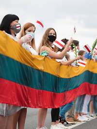 Eine Menschenkette steht mit Fahnen und Blumen hinter einer Stoffbahn in den litauischen Farben.