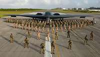 Soldaten stehen in Formation vor einem B2-Bomvber auf einem Flugfeld.