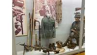 Eine Vitrine mit Waffen, Skiern, Stöcken, Schneeschuhen und einem Seil