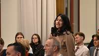 Eine Frau mit Mikrofon die eine Frage an das Podium stellt