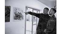 zwei Männer in Uniform vor einer Wand mit Fotos