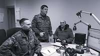 2 männliche Soldaten und 1 Mann an einem Schreibtisch mit Mikrofonen