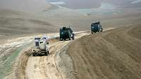 Zwei Fahrzeuge der Bundeswehr und eines der Polizei fahren hintereinander auf einer staubigen Straße