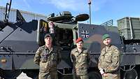 Drei Soldaten stehen in Uniform vor einem Bergepanzer mit geöffneter Seitenluke