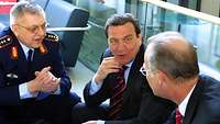 Kujat, Schröder und Scharping sitzen in einer Sitzgruppe und befinden sich im Gespräch.