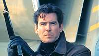 Der Schauspieler Pierce Brosnan schaut als James Bond in die Kamera und hält dabei eine Waffe.