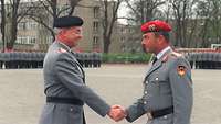Farbfoto von zwei Männern in Uniform, die sich die Hände reichen, im Hintergrund stehen weitere Uniformträger